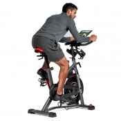 Schwinn IC8 spinningcykel sedd från sidan med användare i aktiv trampställning mot neutralt bakgrund.