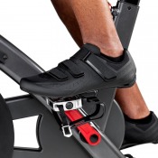 Detaljbild på fot placerad på pedal med justerbar fotkorg och rem i svart plast och metall.