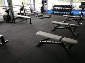 Ett modernt och välutrustat gym med våra högkvalitativa svarta gummigolvplattor i förgrunden. Plattorna skapar en estetisk och f