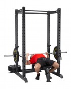 Power rack med bänk och skivstång, med person liggande och tränar, i gymmiljö.