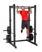 Power rack med person som tränar i ramen med skivstång och röda säkerhetsarmar, i gymmiljö.