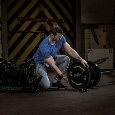 Person med skivstång och svarta bumper plates i mörk träningsmiljö med fokus på viktskivorna.
