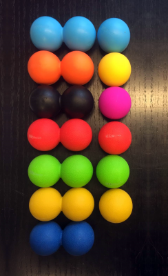 Lacrossebollar i flera färger ordnade i rutnät i svart förpackning mot vit bakgrund.